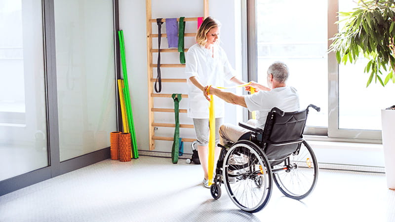 Una mujer joven fisioterapeuta trabajando con un adulto mayor en silla de ruedas. Una mujer joven fisioterapeuta trabajando con un adulto mayor en silla de ruedas.